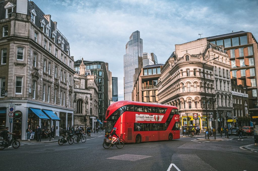 Red double-decker bus traverses a bustling London street showcasing historic and modern architecture.