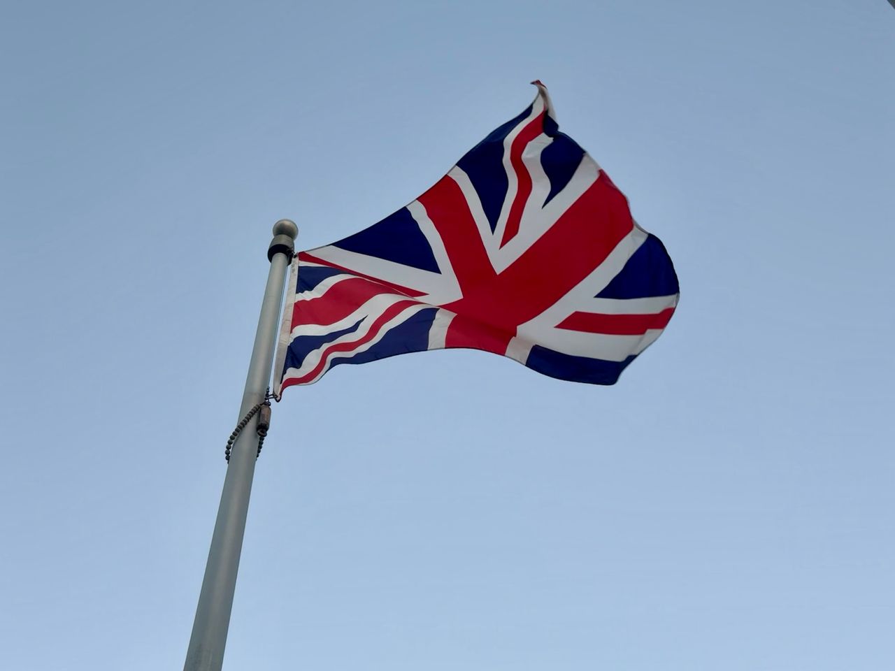 A Union Jack flag waving against a bright blue sky, symbolizing Great Britain.